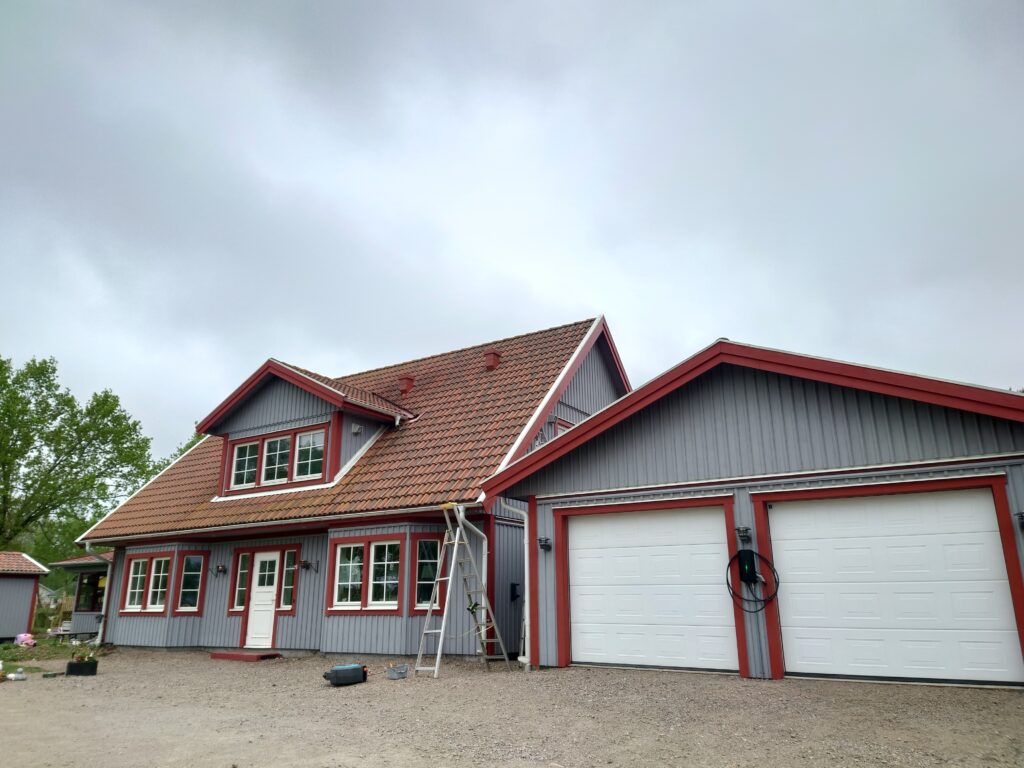 Trähus och dubbelgarage med grå fasad och röda detaljer