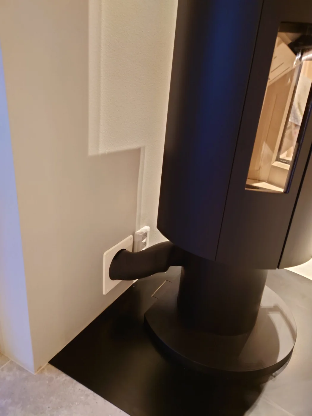 Närbild av anslutning vid en svart kamin intill en vit vägg