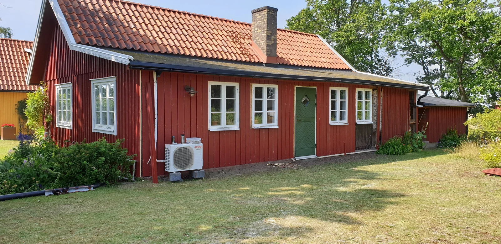 Rött trähus med tegeltak, skorsten och svarta hängrännor