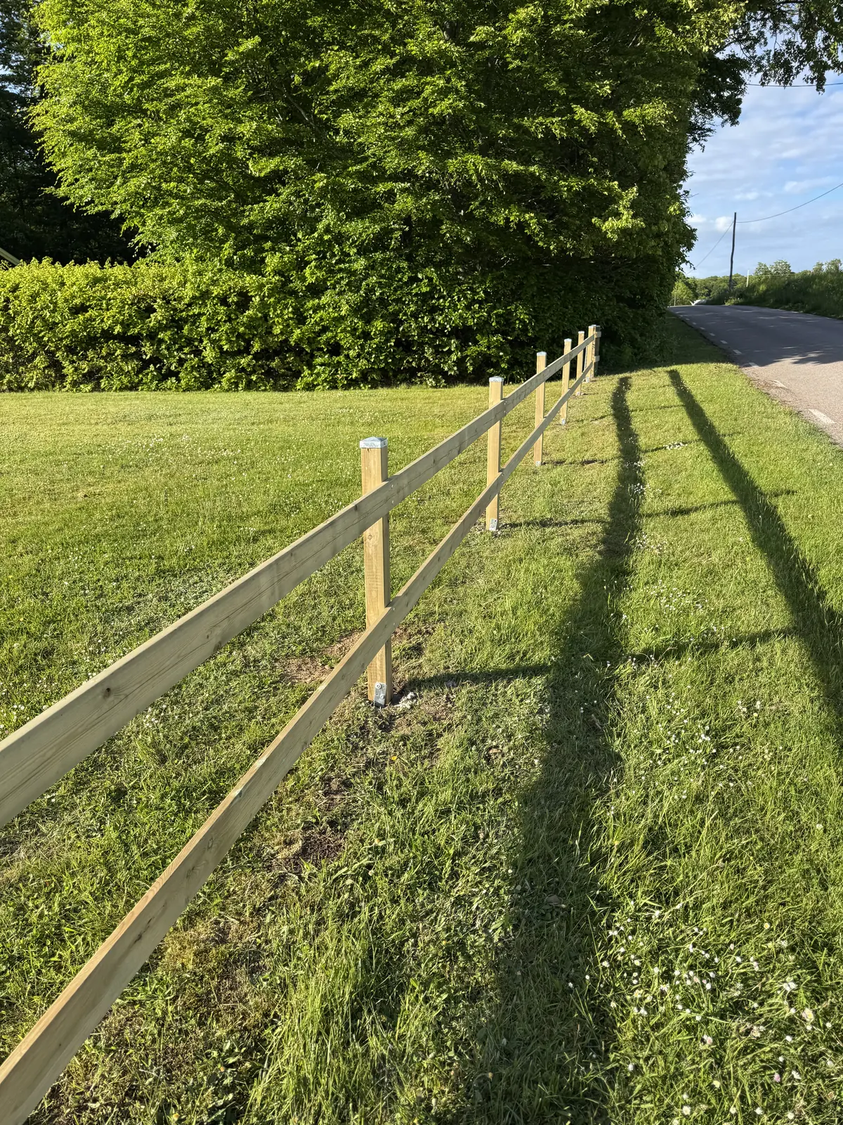 Öppet trästaket med två liggande slanor längs en gräsyta i Döshult