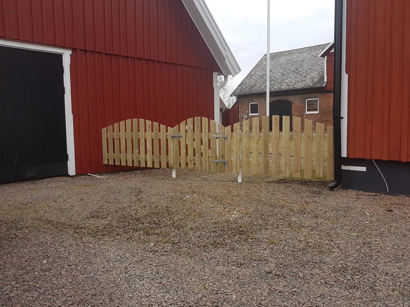 Trägrindar med bågformad överkant mellan röda byggnader i Ausås